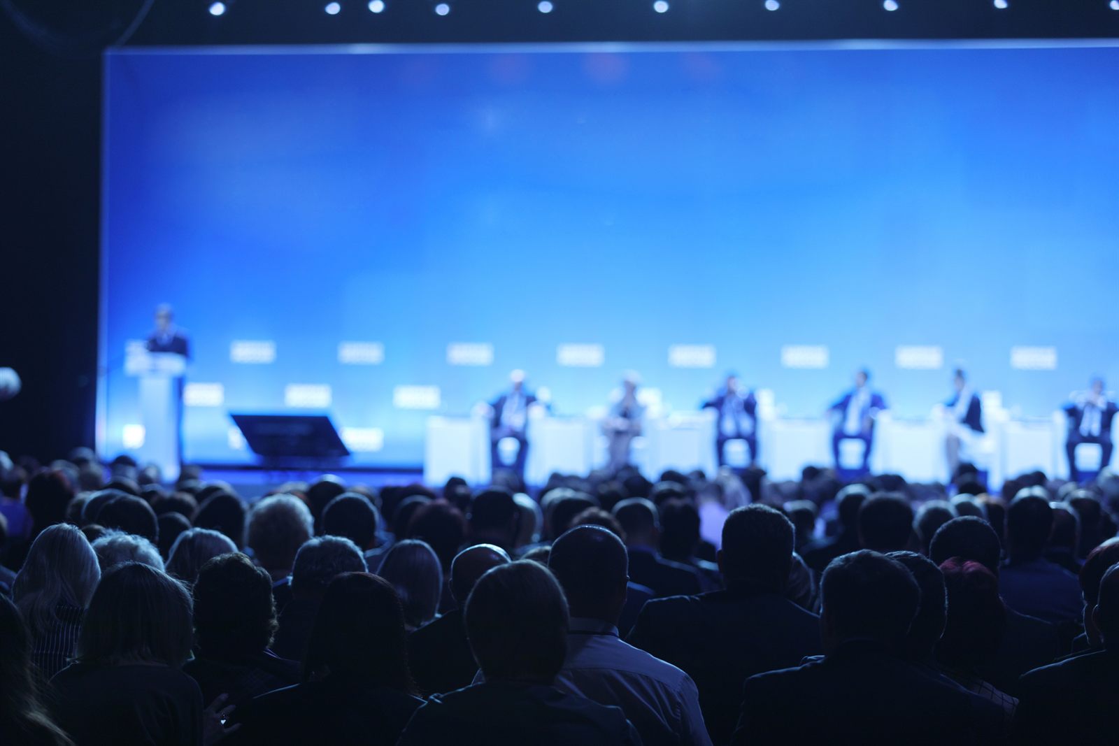 Audience facing a lit stage with a panel of presenters